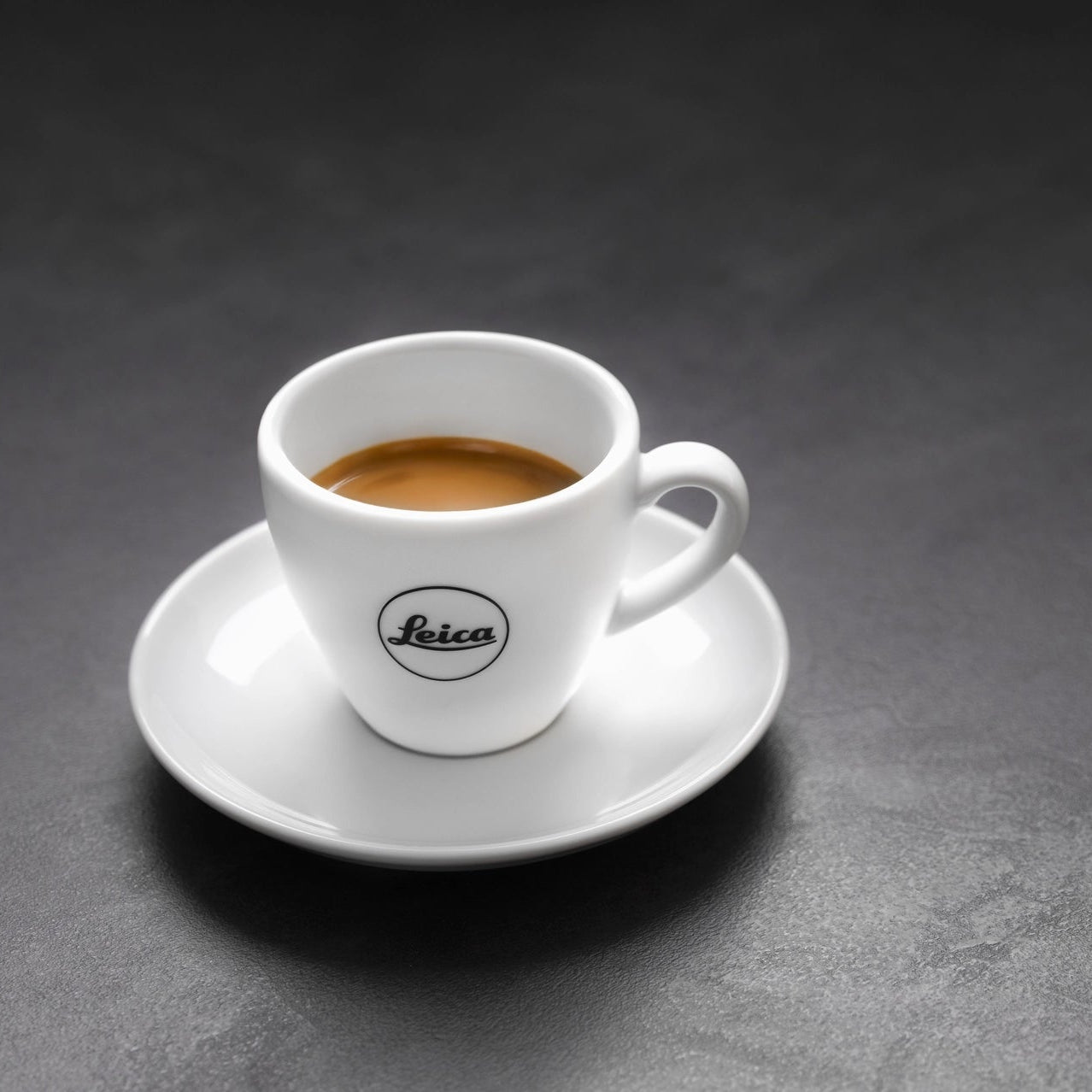 White espresso cup with saucer featuring Leica logo on a dark gray background